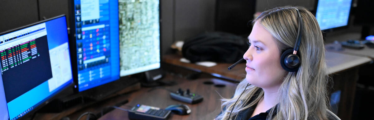 Dispatcher with headset working at multiple computer monitors in a police communications center.