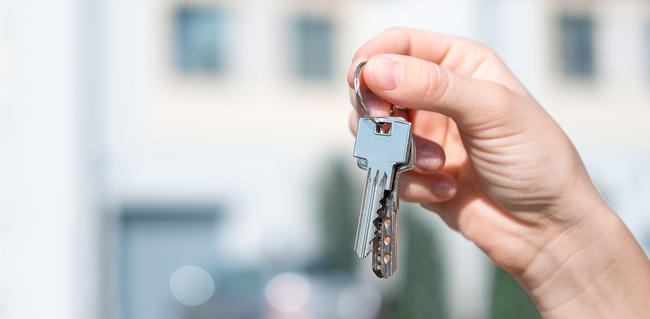 Hand holding key in front of houses