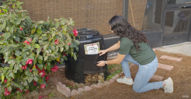 Resident kneeling down to access finished compost on side of compost bin in yard